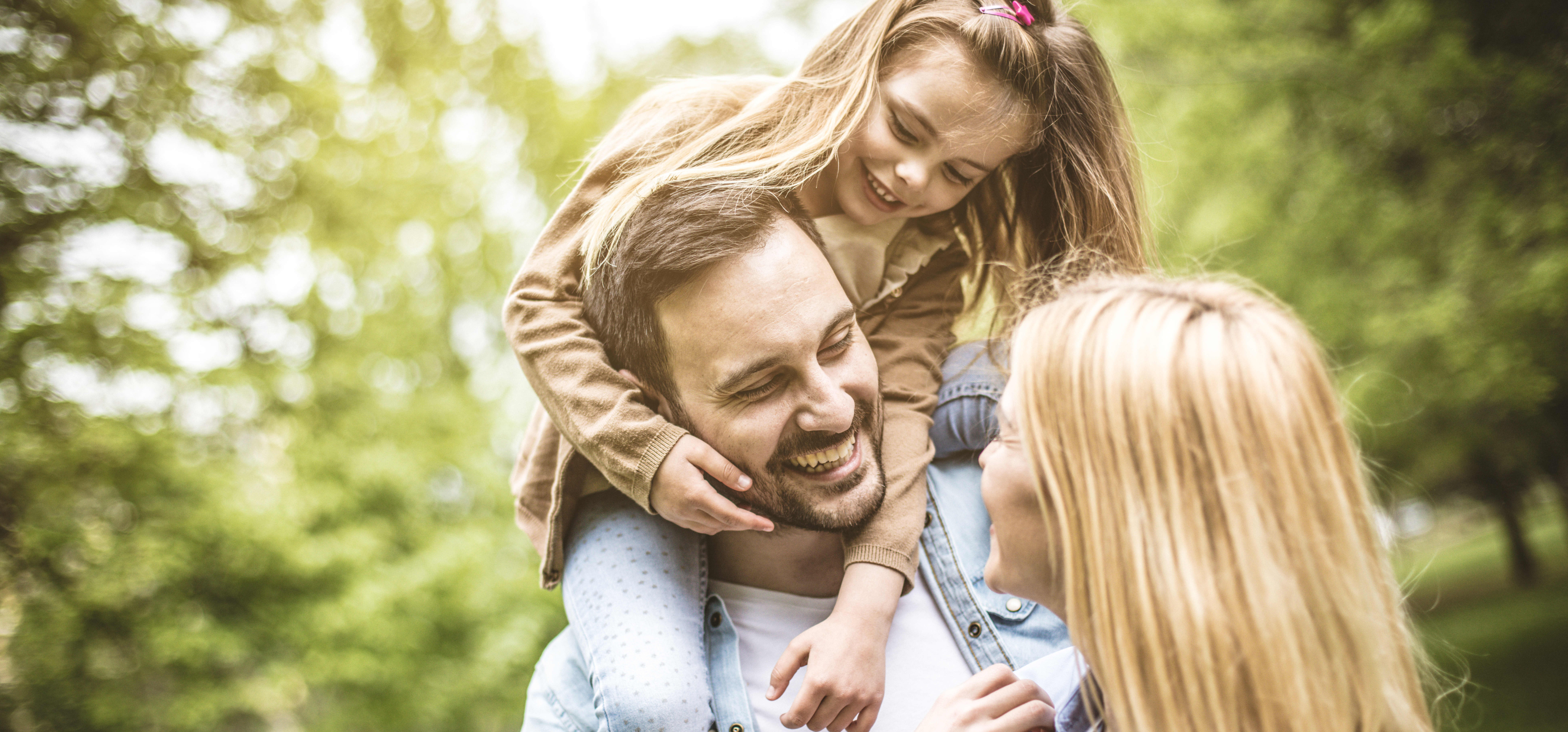 Junges lachendes Paar im Grünen, der Vater hat seine Tochter auf den Schultern