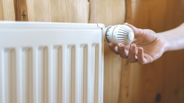 Person dreht am Thermostat eines Heizkörpers