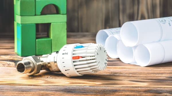 Thermostat neben Bauzeichnungen und grünem Haus