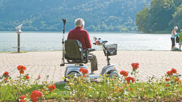 Älterer Mann sitzt auf Elektromobil und genießt den Ausblick aufs Wasser