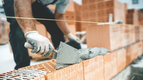 Maurer baut ein Massivhaus und streicht Zement auf Bausteine