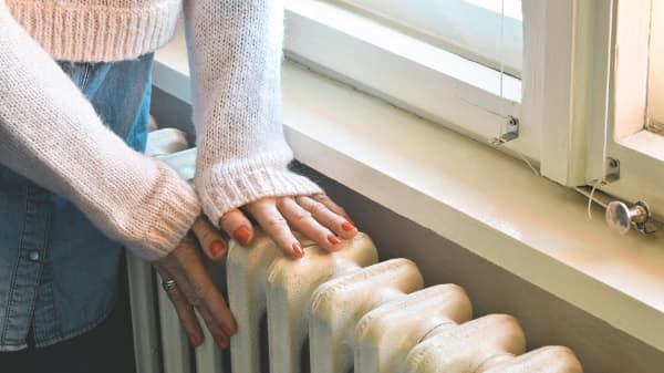 Frau wärmt sich Hände an Heizung