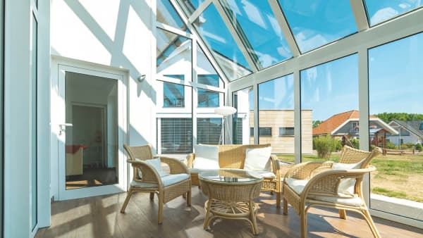 Großer Wintergarten mit weißen Profilen und einer Sitzgruppe aus Korb.