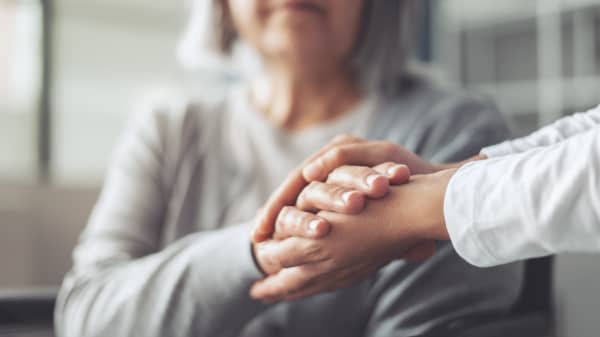Seniorin und jüngere Person halten sich die Hände