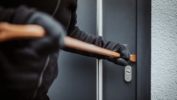 Dunkel gekleideter Einbrecher stemmt eine schwarze Haustür mit einem Brecheisen auf
