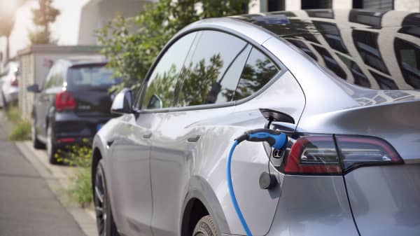 Silbernes Elektroauto am Straßenrand mit eingestecktem Ladestecker