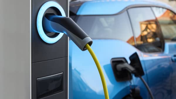 Ladesäule mit angeschlossenem Ladestecker und E-Auto im Hintergrund