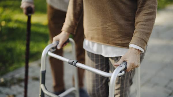 Senior und Seniorin mit Gehhilfe auf gepflastertem Weg