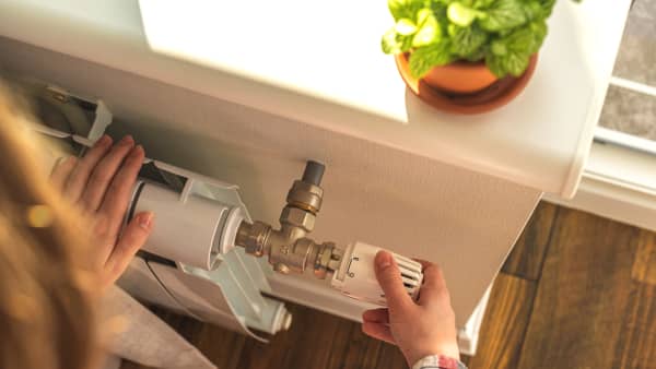 Person dreht das Thermostat eines Heizkörpers