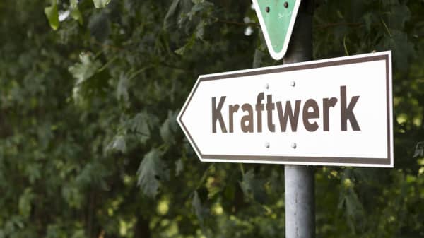 Richtungsweisendes Schild mit der Aufschrift Kraftwerk vor grünen Büschen