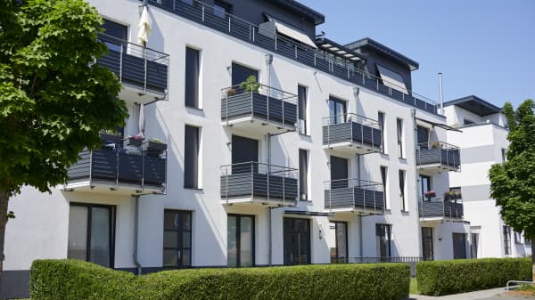 Modernes Mehrfamilienhaus mit weißer Fassade und Balkonen, davor eine gepflegte, grüne Hecke