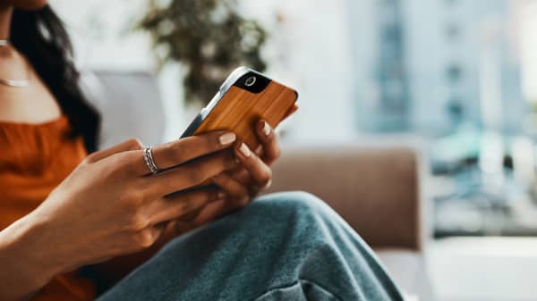 Junge Frau mit Smartphone in der Hand sitzt in Wohnung