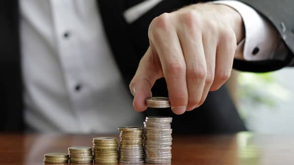 Mann in Hemd und Sakko stapelt Münzen auf ansteigend hohe Stapel auf einem Tisch