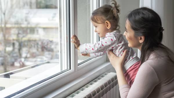 Mutter und Kleinkind schauen aus einem Fenster in einer Wohnung