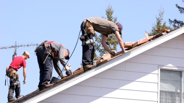 Drei Handwerker machen eine energetische Sanierung auf einem Hausdach