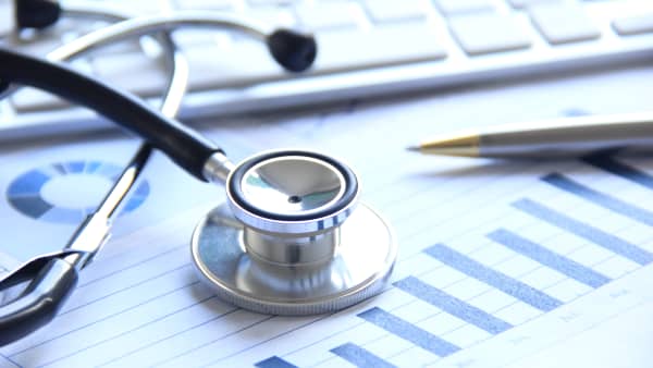 Stethoskop, Kugelschreiber, Finanzübersicht und Computertastatur auf einem Tisch