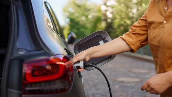 Person in brauner Bluse steckt Ladekabel in ein schwarzes Elektroauto