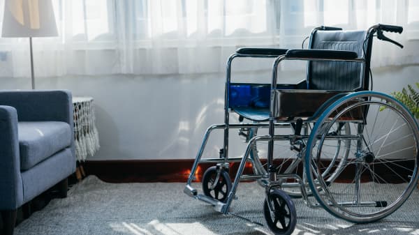 Rollstuhl auf einem Teppich neben einem blauen Sessel vor einem Fenster