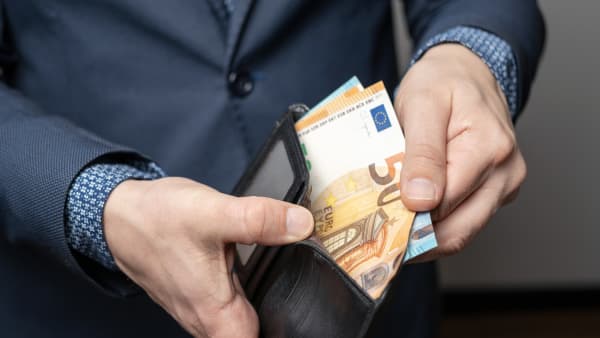 Älterer Mann im Anzug öffnet eine Geldbörse mit mehreren Geldscheinen