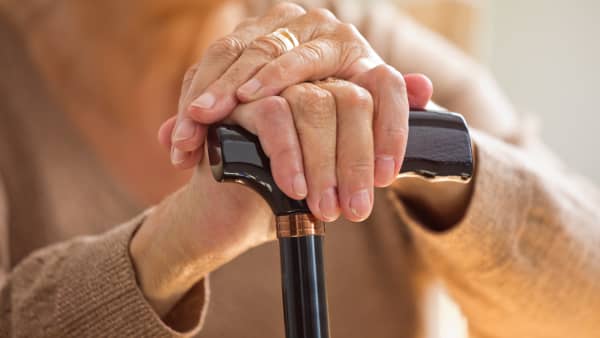 Seniorin hält einen Gehstock fest, der Fokus liegt auf ihren Händen