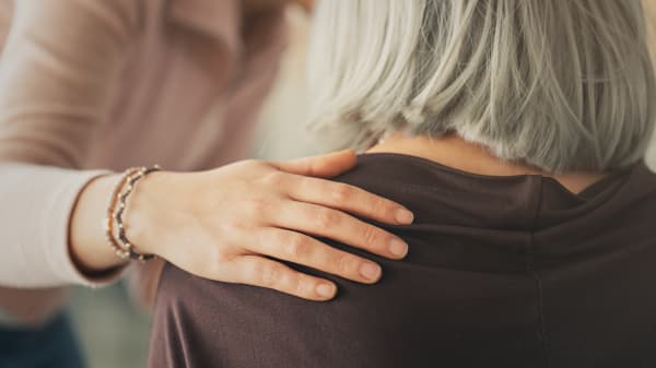 Jüngere Frau legt einer Seniorin mit kurzen grauen Haaren eine Hand auf die Schulter