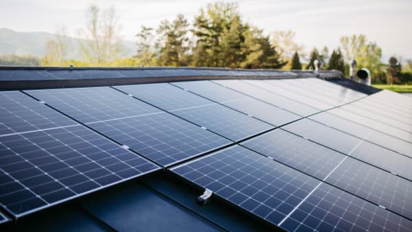 Solarmodule auf einem Schrägdach mit grünen Bäumen und Himmel im Hintergrund