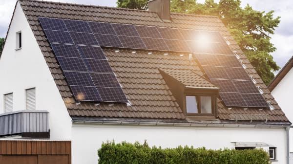 Wohnhaus mit weißer Fassade, brauner Dacheindeckung und Solarmodulen, auf die die Sonne scheint