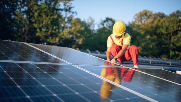 Monteur mit roter Arbeitshose und gelbem Helm montiert eine Solaranlage auf dem Dach