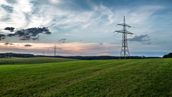Strommasten auf grüner Wiese vor bewölktem Himmel