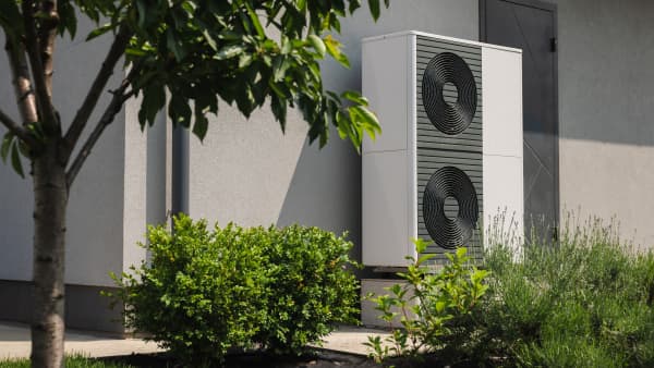Moderne Wärmepumpen an der Fassade eines Wohnhauses mit grünem Garten