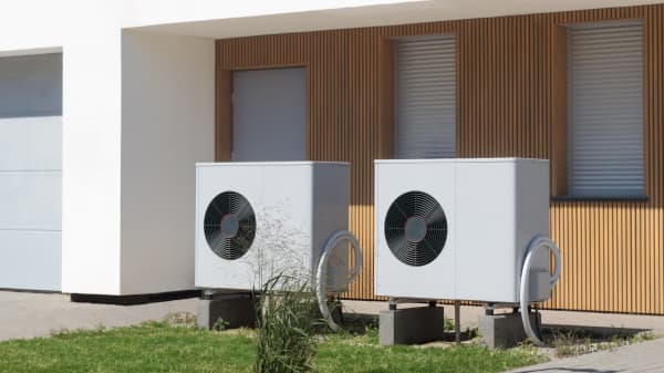 Zwei Luftwärmepumpen auf kleiner Rasenfläche vor Haus mit Holzvertäfelung an der Fassade