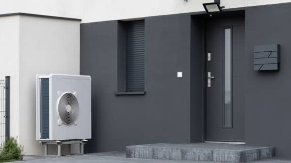 Weiße Luft-Wärmepumpe auf Sockel steht an modernem, dunklem Wohnhaus