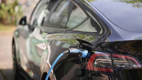 Ansicht eines schwarzen Elektroautos von hinten links mit angeschlossenem Ladekabel