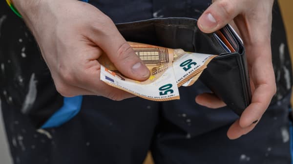 Ein Handwerker hält Geld und ein Portemonnaie in den Händen.