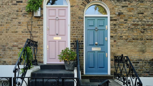 zwei nebeneinanderliegende Haustüren im Landhausstil in sanftem Rosa und beruhigendem Blau vor einer Backsteinfassade