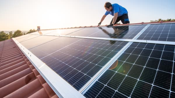 Handwerker installiert Solarmodule auf einem Schrägdach mit Ziegeln bei strahlendem Sonnenschein