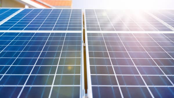 Nahaufnahme von blauen Solarmodulen mit einem klaren Rastermuster, beleuchtet von hellem Sonnenlicht. Die Module gehören zu einer Solaranlage auf einem Wohnhaus und erzeugen erneuerbare Energie zur nachhaltigen Stromversorgung.