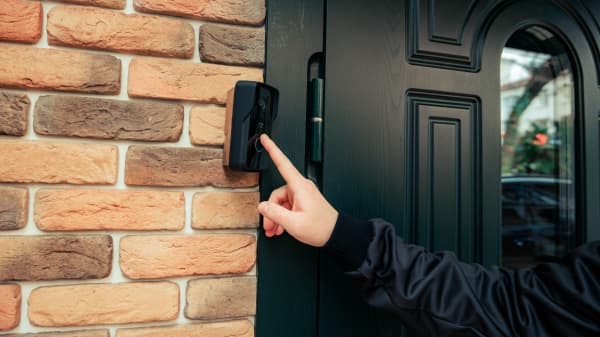 Dunkel gekleidete Person klingelt an der schwarzen Haustür eines Wohnhauses