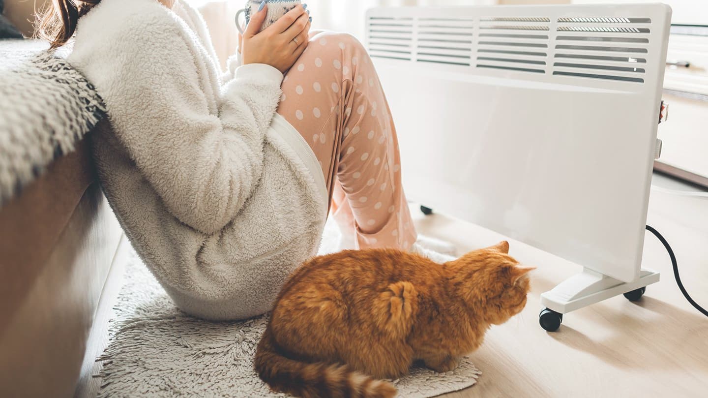 Frau und Katze sitzen vor Heizung