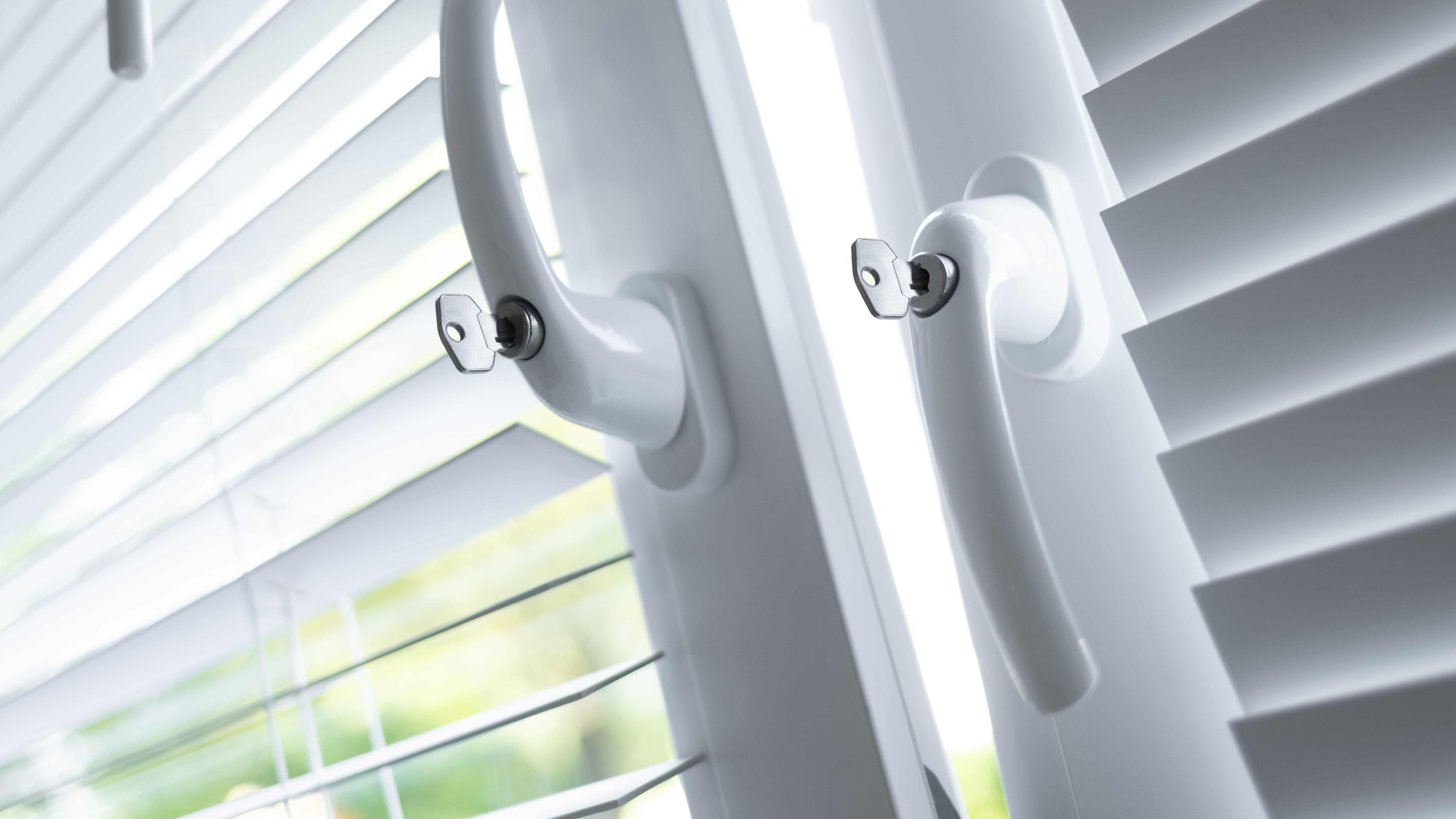 Zwei Fenster mit weißen Rollos und Sicherheitsgriffen, davon ist das linke gekippt