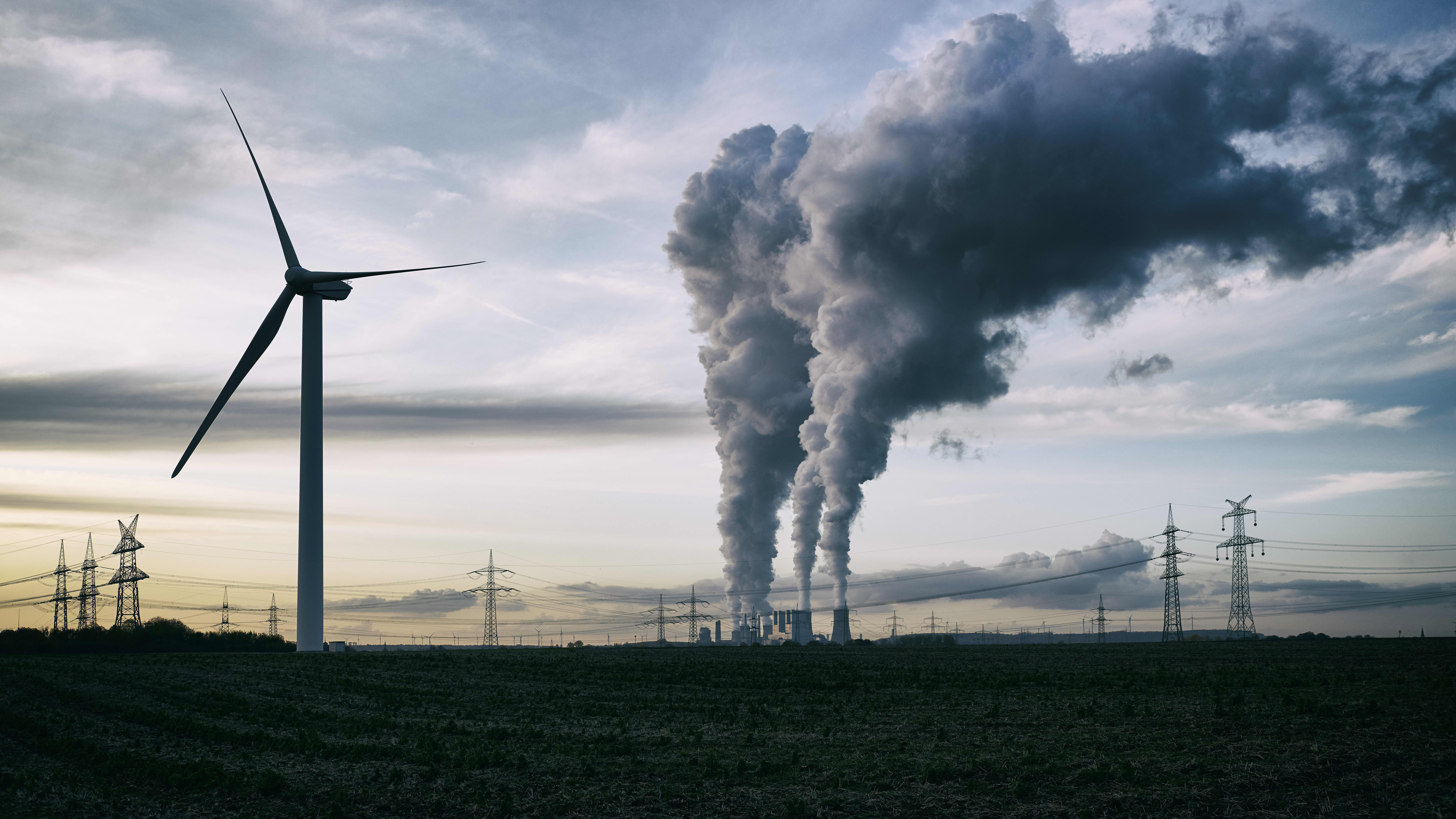 Windrad vor bewölktem Himmel, im Hintergrund Strommasten und ein Kraftwerk