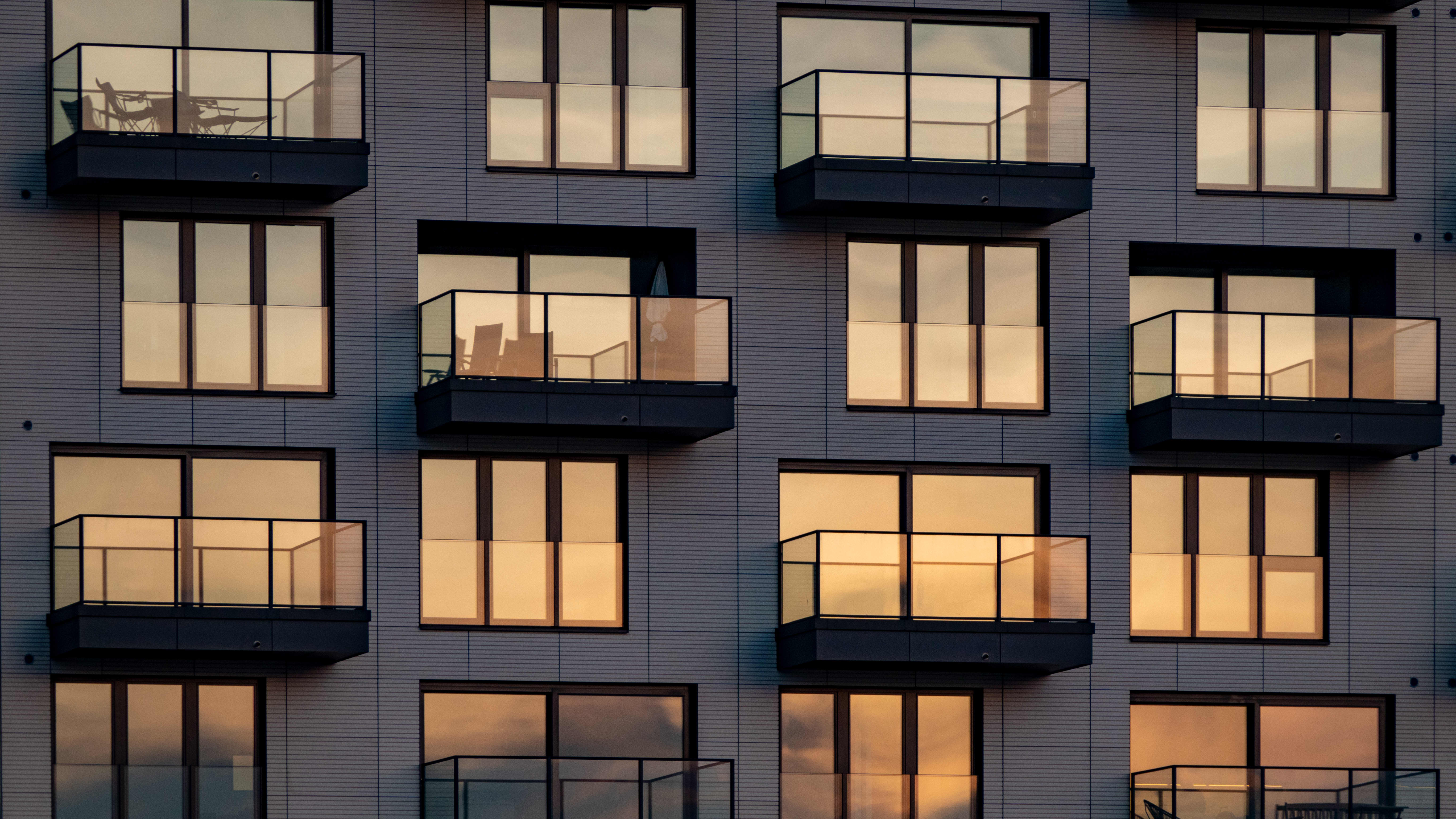 Abendsonne spiegelt sich in Fenstern und Balkonverglasungen an einem modernen Mehrfamilienhaus