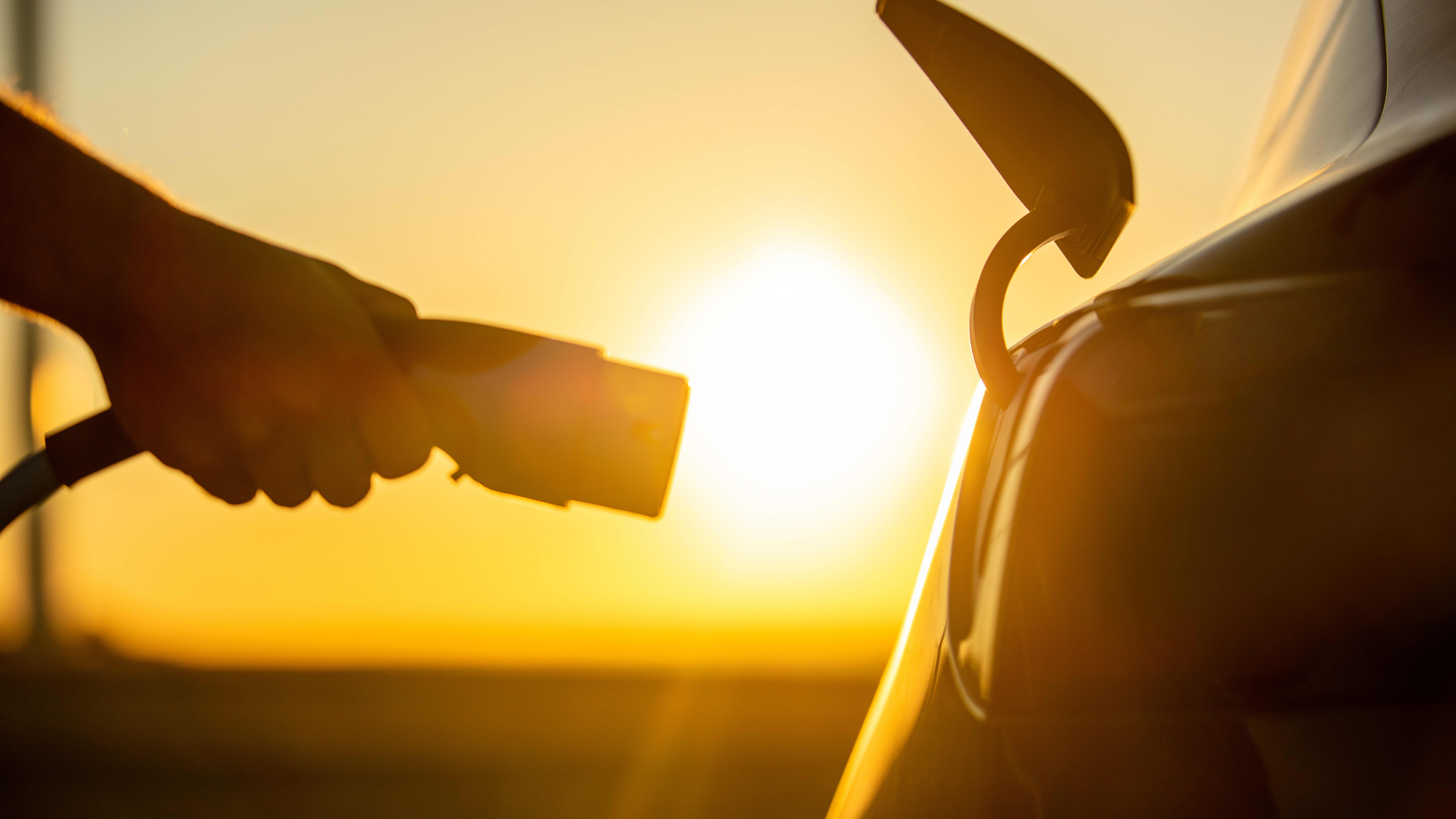 Person steckt bei Sonnenuntergang einen Ladestecker in ein E-Auto