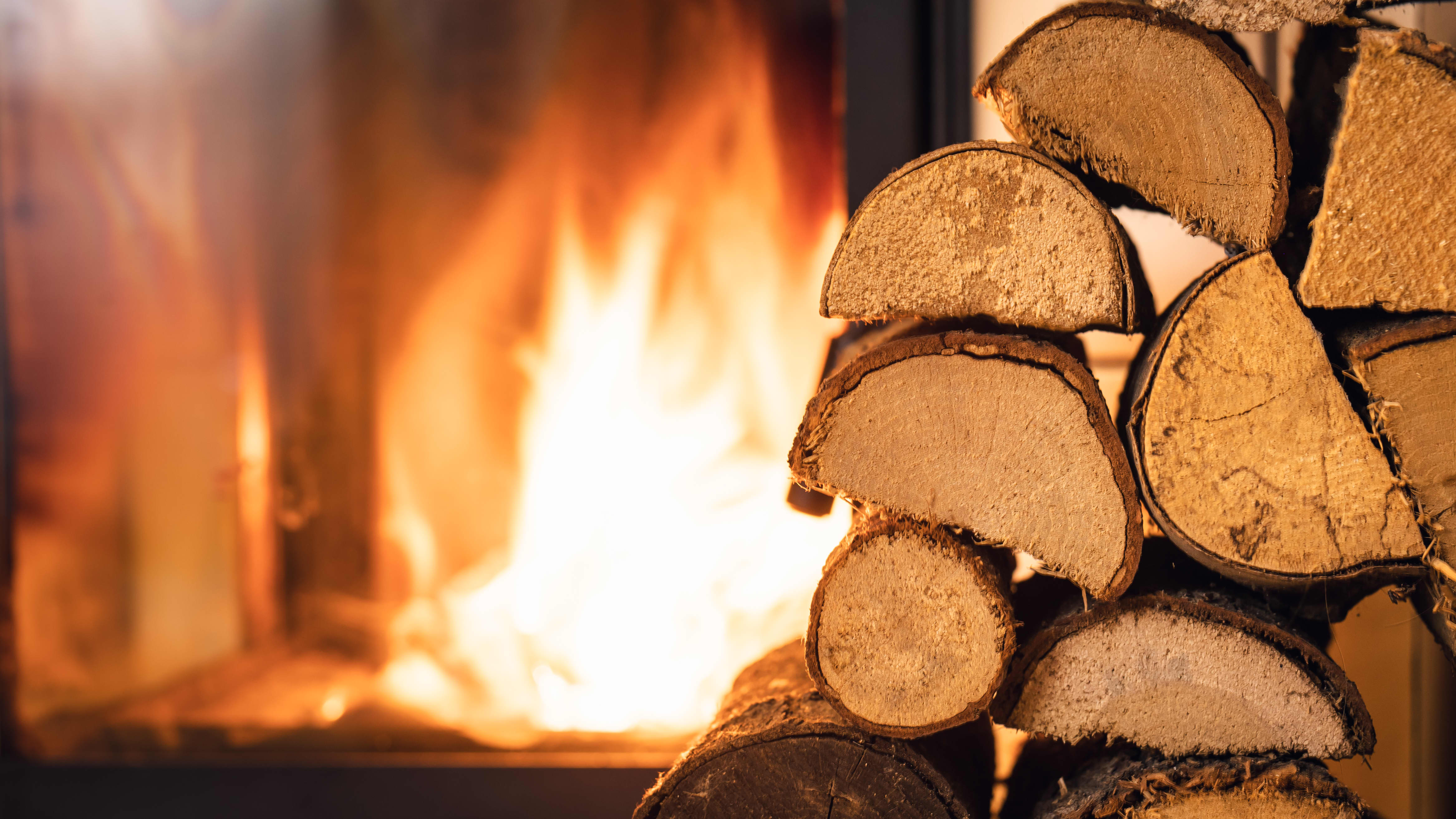 Aufgestapelte Holzscheite vor einem brennenden Kamin