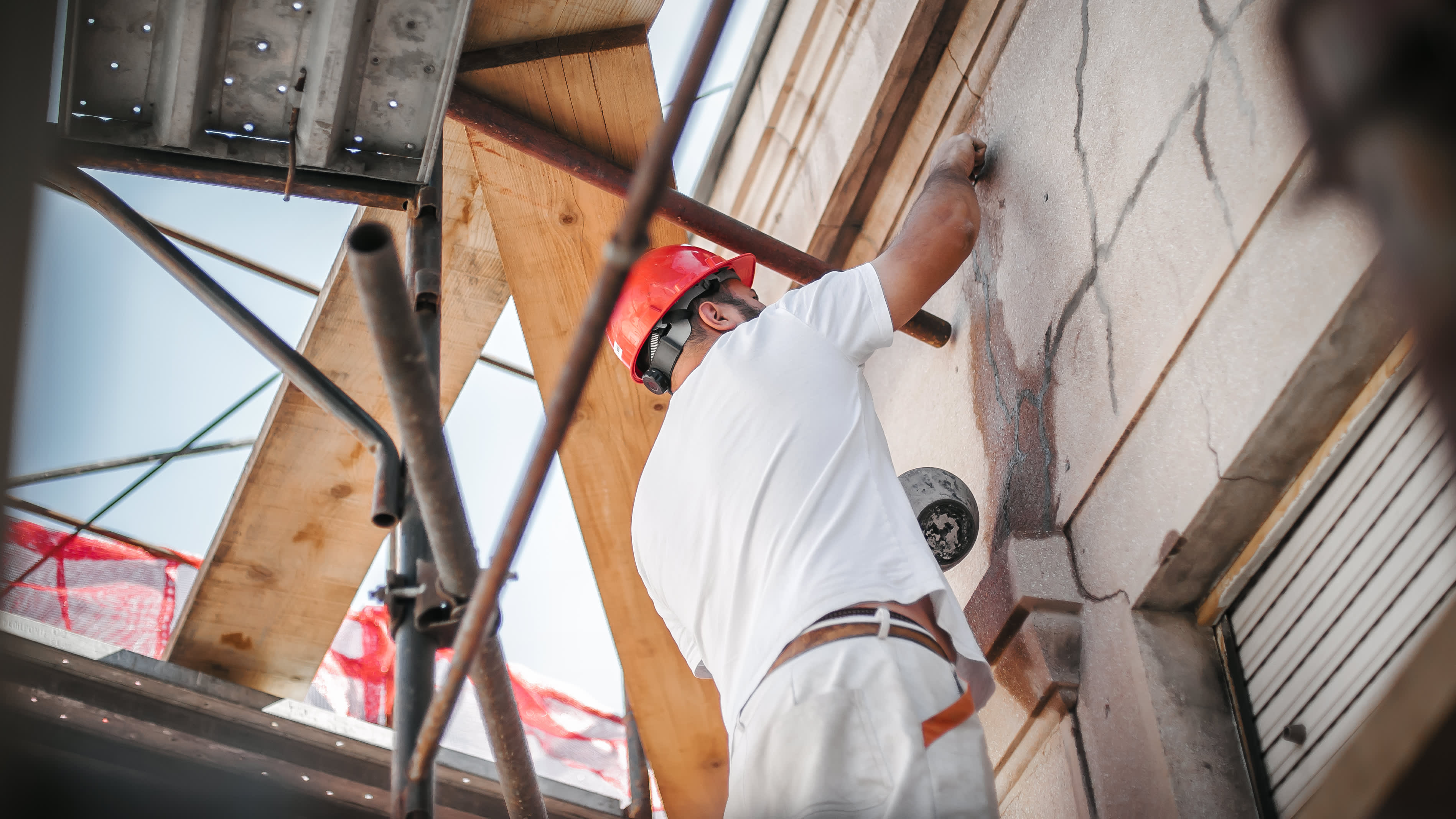Ansicht eines Handwerkers mit weißer Kleidung und rotem Helm, der an einer Fassade arbeitet