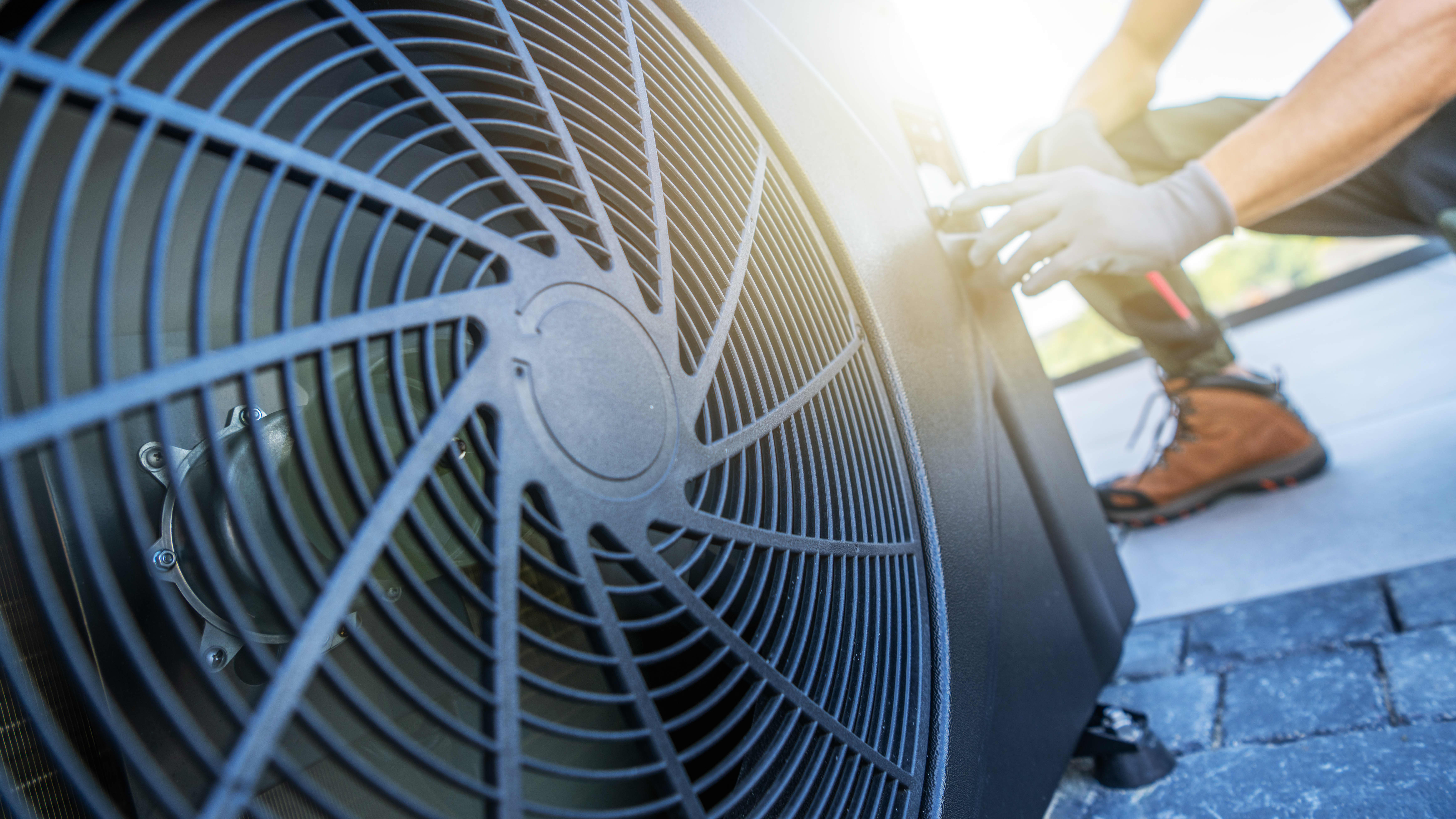 Ein Techniker führt Wartungsarbeiten an einer Klimaanlage auf einem Dach durch. Die Sonne scheint hell im Hintergrund