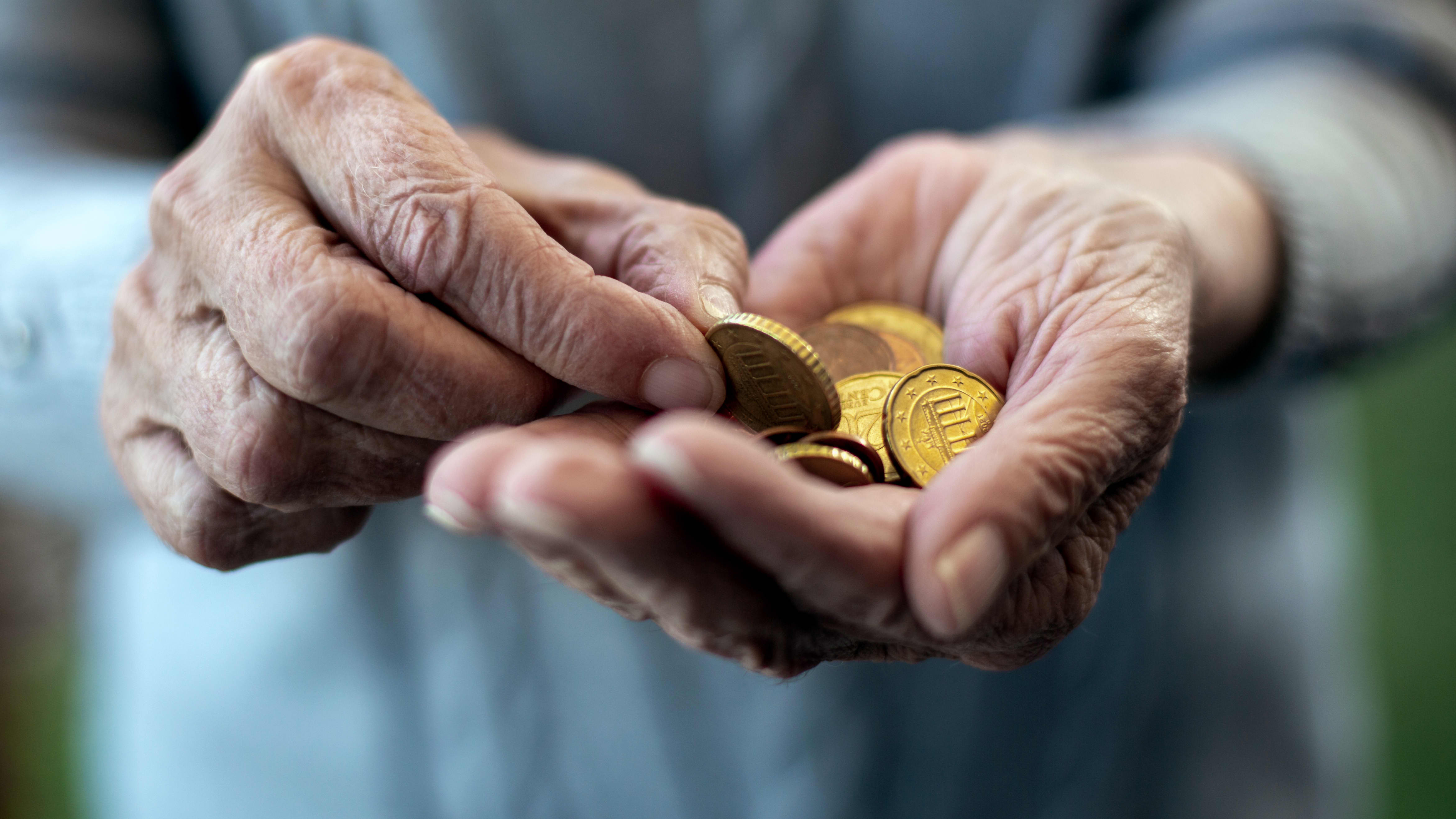 Nahaufnahme der Hände einer älteren Person. Sie hält Euromünzen in der Hand.