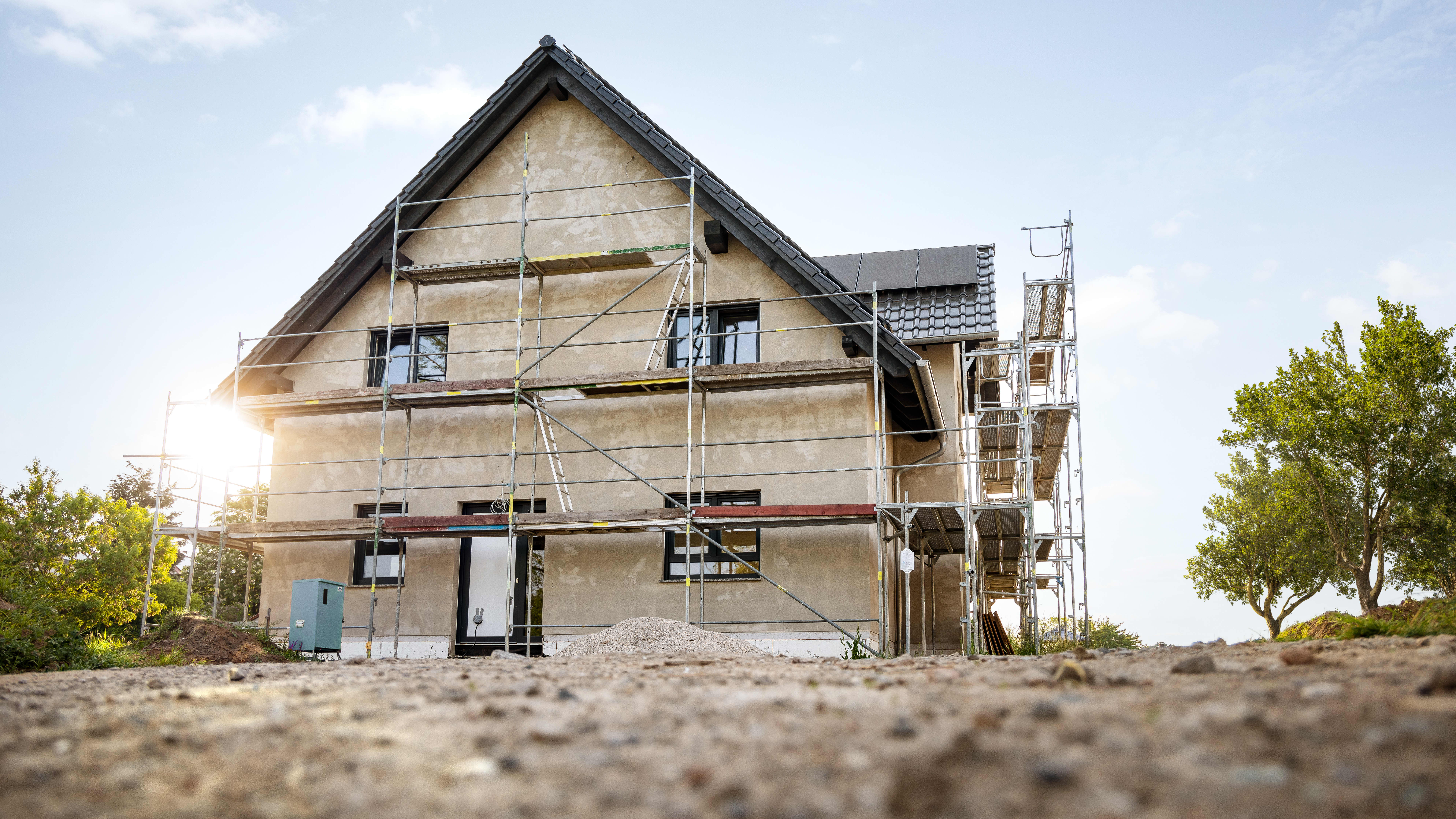 Haus mit Gerüst auf unbepflanztem Boden bei blauem Himmel