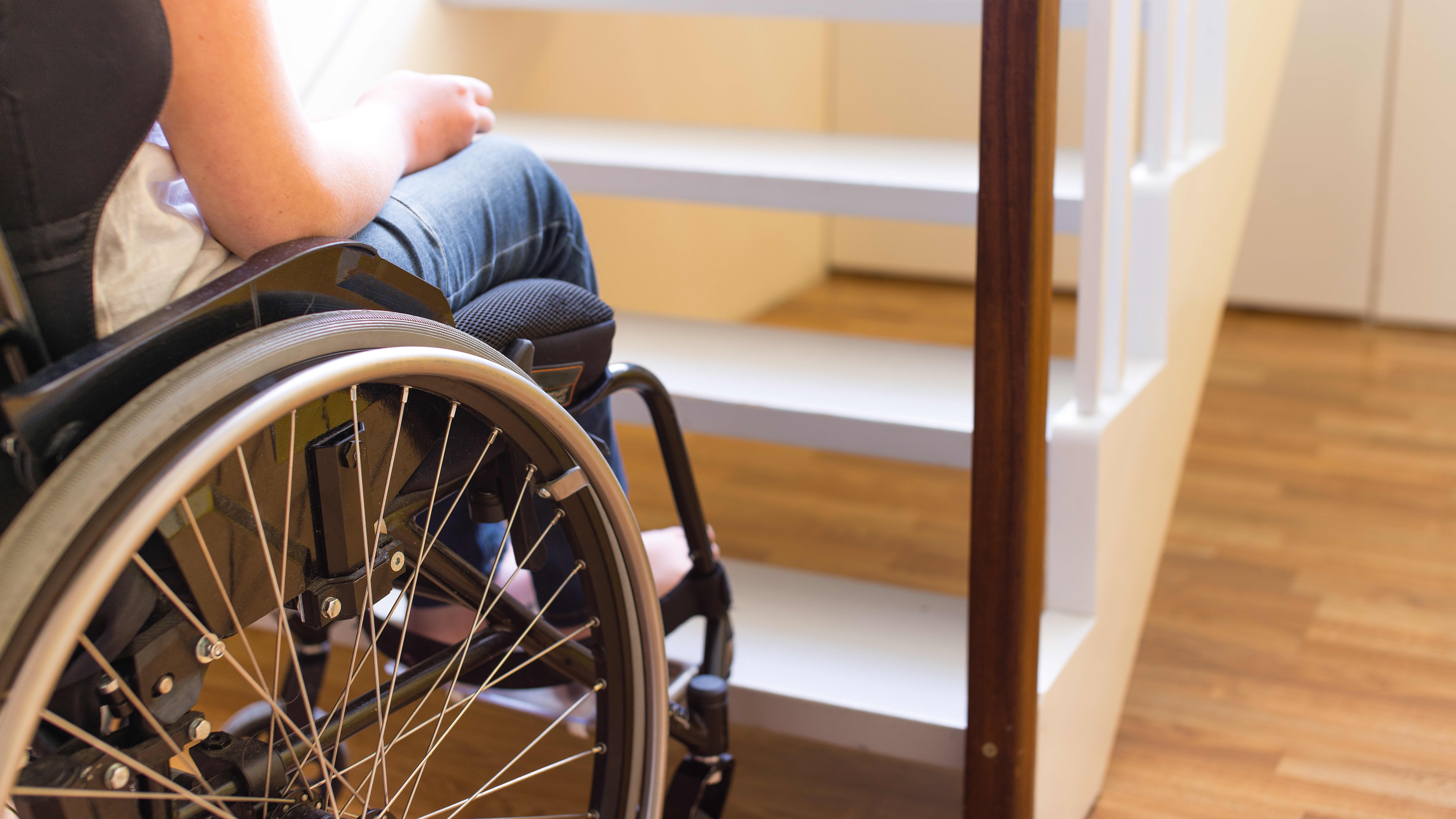 Nahaufnahme einer Person im Rollstuhl am Fuß einer Treppe von hinten