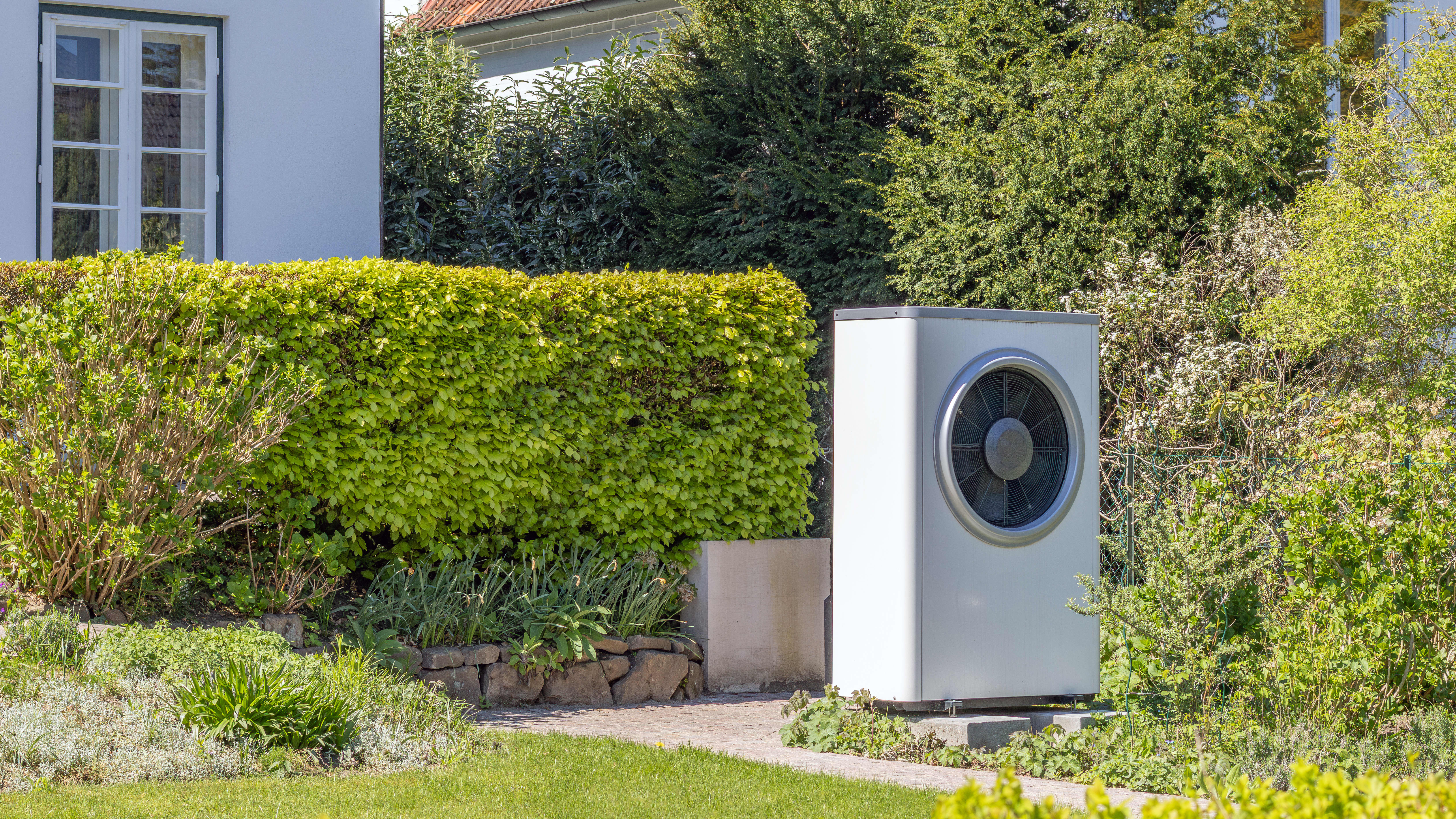 Wärmepumpe im Garten vor einem Haus im Grünen